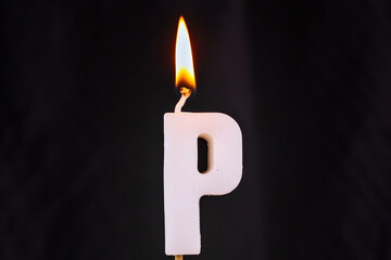 close up on a white letter P birthday candle with fire on a black background.

