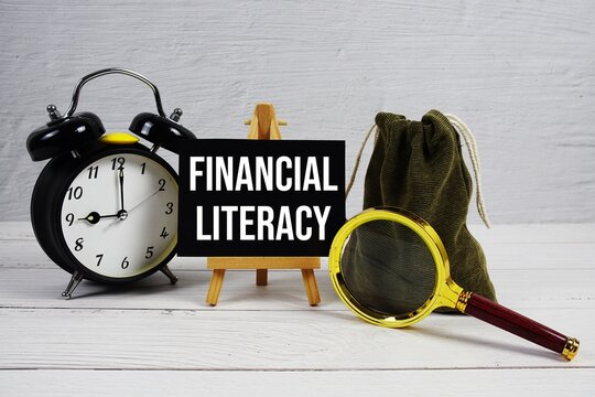 Financial Literacy text with alarm clock and magnifying glass on wooden background