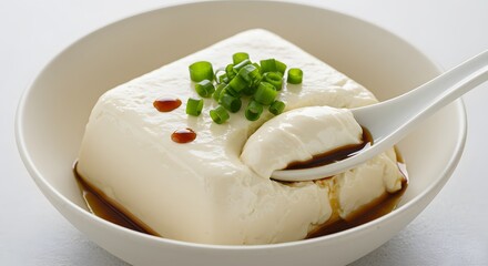 AI image features a block of delicate silken tofu served in a bowl, garnished with green onions and drizzled with soy sauce.