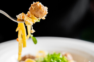A close-up of a fork with pasta, meatball, and fresh vegetables, highlighting textures and colors....