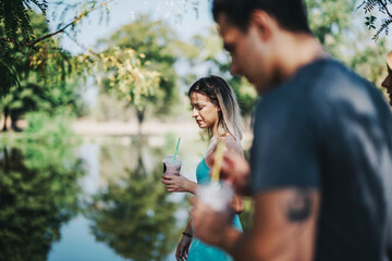 Naklejka premium A group of friends relax in a park, enjoying drinks on a sunny day. The serene environment and lush greenery provide a tranquil backdrop for their casual outing.