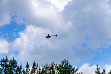 helicopter flying against a partly cloudy sky, with treetops visible at the bottom of the frame. The composition emphasizes themes of aviation, aerial transport, and air surveillance. Suitable for ill
