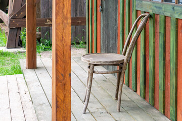 single worn wooden chair standing on a weathered porch beside a colorful wooden fence. The rural...