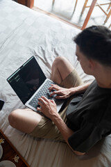 Close-up of a handsome man sitting on bed working on computer, taken from all directions.