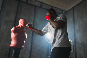 Fitness workout in gym. Strong African man fighter training punches with hitting punching bag...