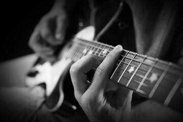 Man playing guitar in darkness, closeup. Black and white effect