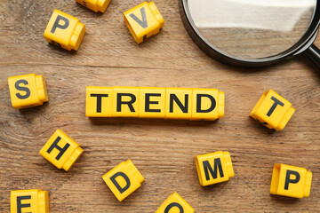Word Trend made of yellow cubes with letters and magnifying glass on wooden background, top view