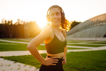 Beautiful woman in sportswear warming up before workout at sunset. Sportswoman listening to music...