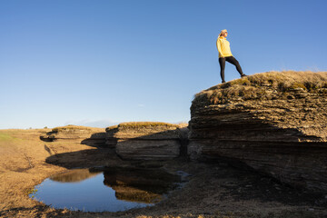 Estonian nature in early spring: a female traveler on top of a rocky hill admiring the landscape with a small lake and blue sky.