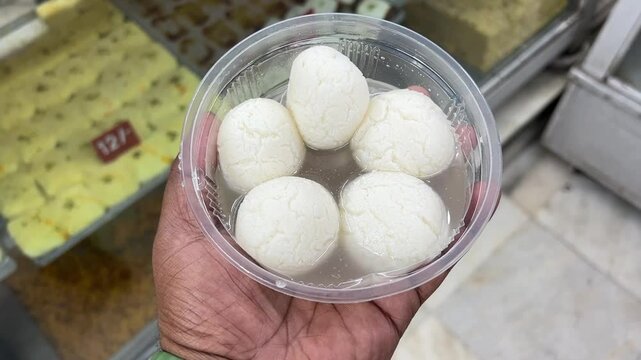 Rosogolla in hands with different Bengali sweets in the background.