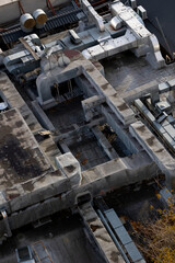 Rooftop featuring various HVAC systems and ductwork including large ventilation units, cylindrical vents with protective covers, and rectangular ducts. The surface of with patches and scattered debris