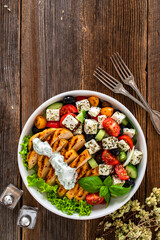 Grilled sliced chicken breast and Greek salad on wooden table	