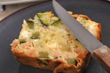 Tranche de cake salé à la feta et aux légumes fait maison dans une assiette avec un couteau en...