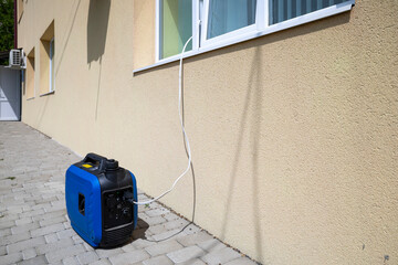 Portable blue generator on a paved surface, connected via a power cable entering through a window...