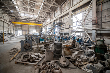 Cluttered industrial warehouse with many electric motors, pumps, barrels, and machinery scattered...