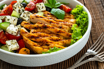 Grilled sliced chicken breast and Greek salad on wooden table	