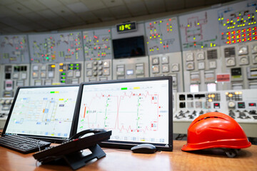 Control room for monitoring and managing industrial operations, with various control panels, analog and digital displays, buttons, and switches. A computer monitor displays graphs and data.