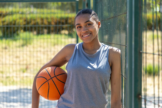 Young female basketball player smiling and holding ball on court