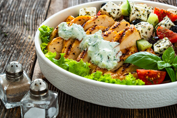 Grilled sliced chicken breast with tzatziki sauce and Greek salad on wooden table	