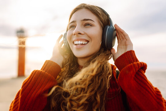 Young woman enjoying the seascape and listening to music with wireless headphones. Relaxed woman with headphones and phone at sunset. Freedom and relaxation concept.
