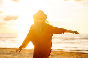 Cute woman in hat feeling freedom and enjoying sunset on beach. Portrait of woman in stylish...