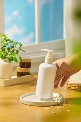 The shampoo bottle was held lightly in the air by a hand. Daisies and flower petals scattered around for decoration. Amber bottles were stacked on top of each other, next to a pot of green leaves.