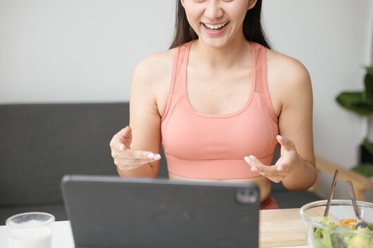 Healthy woman preparing organic fruit and vegetable salad in kitchen for healthy lifestyle during video calling and live streaming via tablet on social media - Powered by Adobe