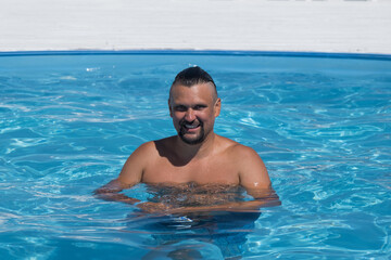 A man in sunglasses swims in a blue pool. Vacation at the hotel by the sea, sunset and mountains. Happy dad, family happiness. Muscles and a beautiful figure, black hair. High quality photo