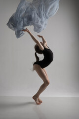 A girl in a swimsuit and a dress shows beautiful athletic elements on a white background. Ballet, rhythmic gymnastics, fabric, aesthetics, grace