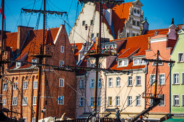 Scenic view of Gdansk's historic architecture, showcasing colorful, traditional buildings with red-tiled roofs. A tall ship mast enhances the city's rich maritime history charm