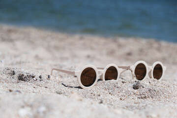 Two pairs of white round sunglasses that are lying on the beach. Blue sea and sun-protected crepe, warm weather, vacations, travel.High quality photo