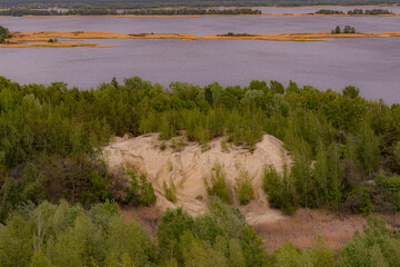a sandy hill covered with trees on the bank of a river