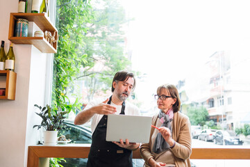 Cafe owner consults with financial adviser using laptop in a bright cafe setting. They collaborate...