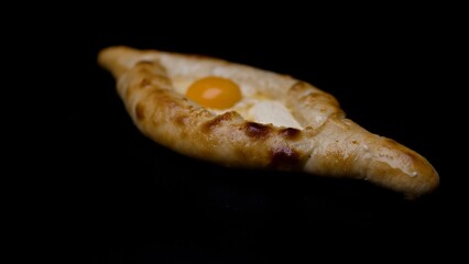 Adjarian khachapuri, a traditional georgian dish, rotates slowly against a dark backdrop, showcasing its golden crust and single egg