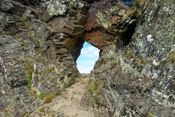 A small hole in a rock wall with a blue sky in the background