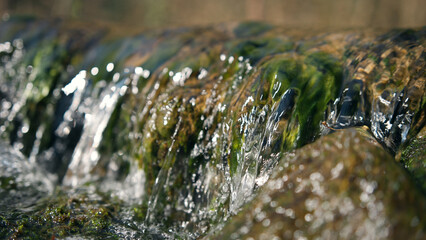 Sunny stream closeup view in the forest. Clean river flowing through stone boulders.
