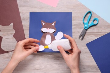 Woman making postcard with cat at wooden table, top view. Child handmade craft