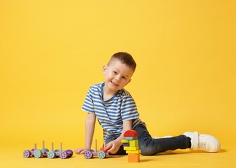 Naklejka premium Cute little boy playing with train toy on yellow background
