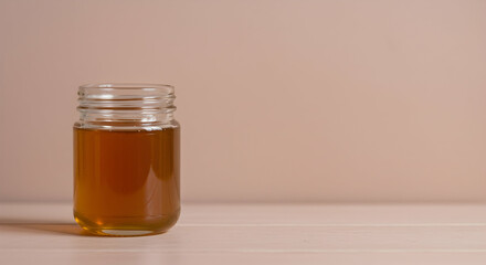 Transparent Glass Jar Filled with Golden Liquid on Light Background