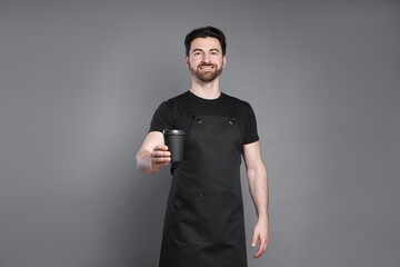 Portrait of smiling barista with paper takeaway cup of hot drink on grey background