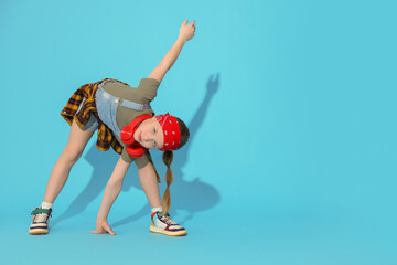 Girl with headphones dancing on light blue background, space for text