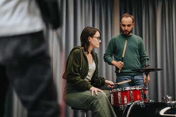 A group of individuals working together during a musical practice session, focusing on a drum kit. The image showcases collaboration and teamwork in a professional artistic studio environment.