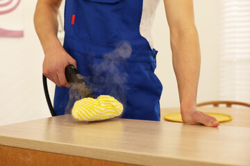 Janitor cleaning wooden surface with steam cleaner at home, closeup