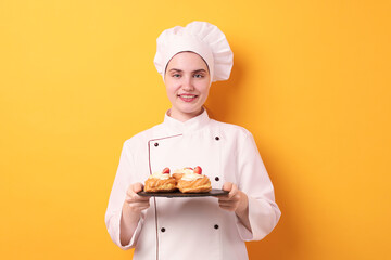 Confectioner in uniform holding delicious profiteroles on orange background
