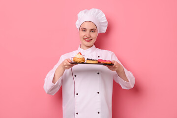 Confectioner in uniform holding different delicious desserts on pink background