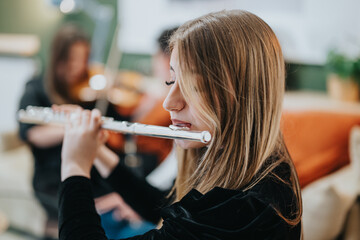 A young female musician performs on the flute as part of a group practice in a cozy indoor setting....
