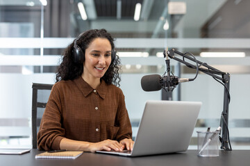 A smiling woman with headphones is using a laptop, likely for a podcast recording or live stream.