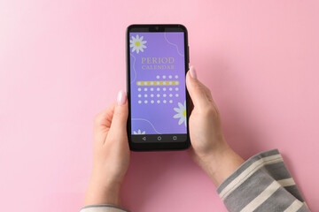 Menstruation. Woman holding smartphone with period calendar application on pink background, top view