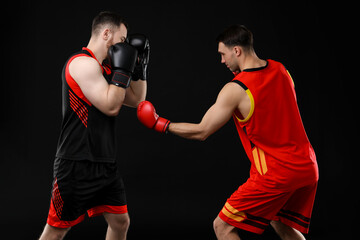 Men in boxing gloves fighting on black background