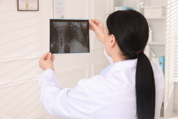 Doctor examining neck MRI scan in clinic, back view
